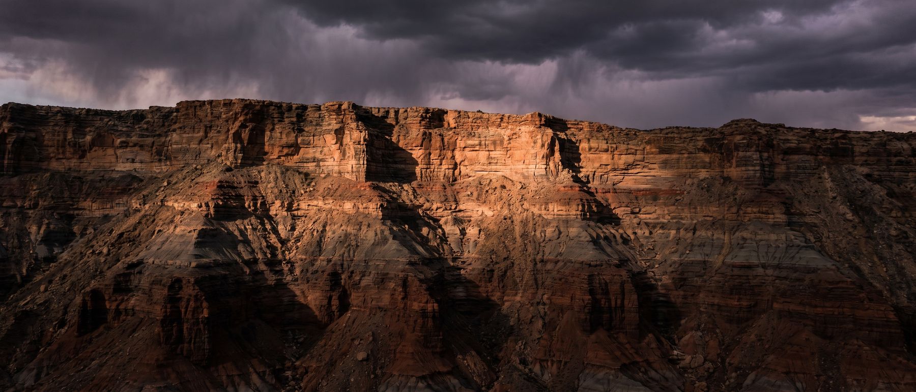 A deep-cut cliff face of layered sedimentary rock, each band lit separately